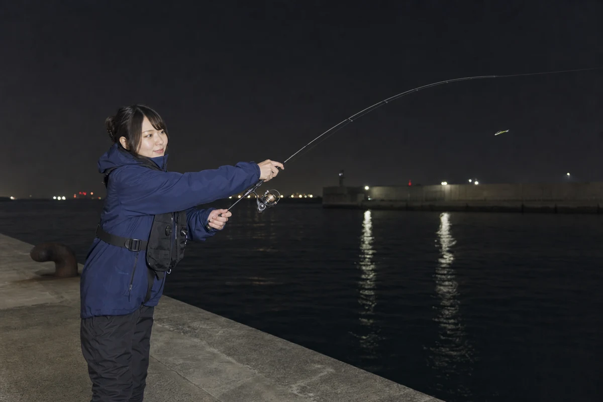 夜の堤防から軽いメバリングロッドで海へキャストする女性
