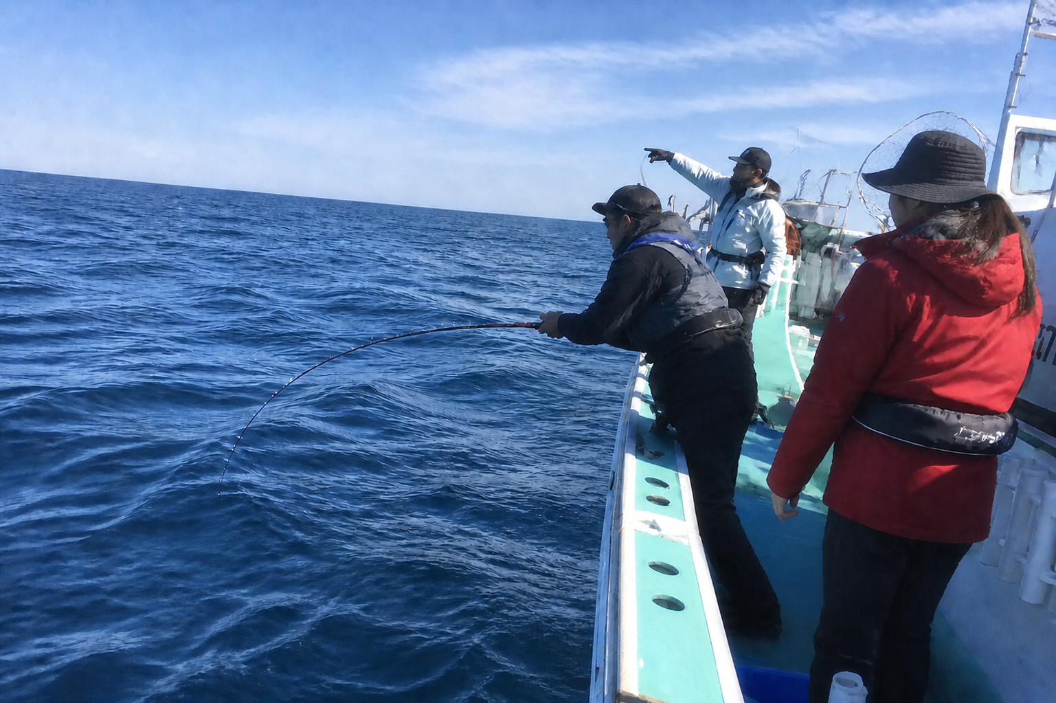 船長の指示と隣の釣り人のヒットを見ている船上の釣り人