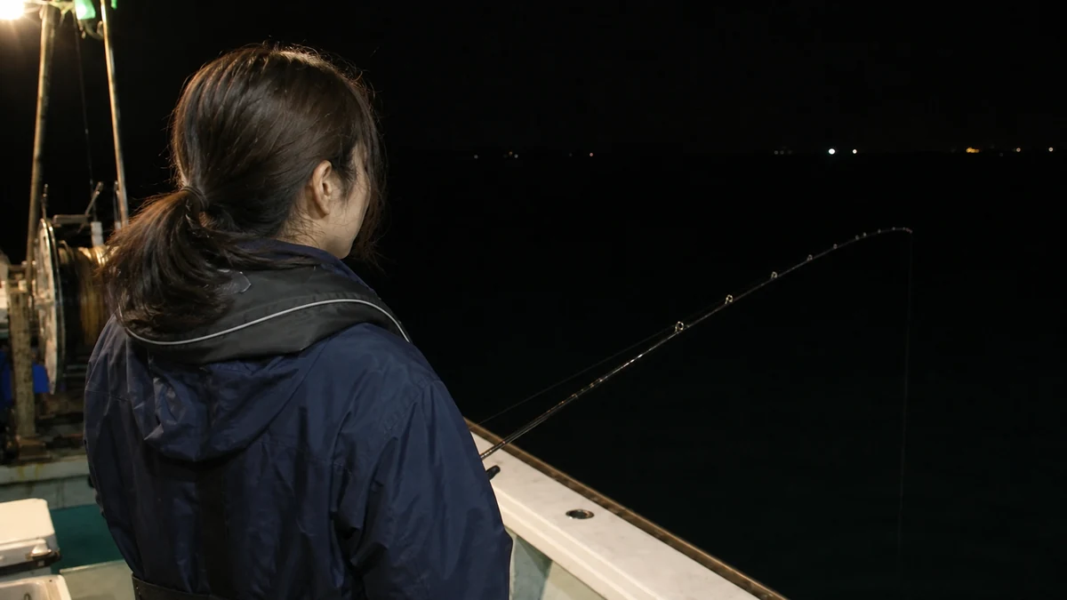 夜の船上で女性がロッドを止め、穂先の変化を見ている様子
