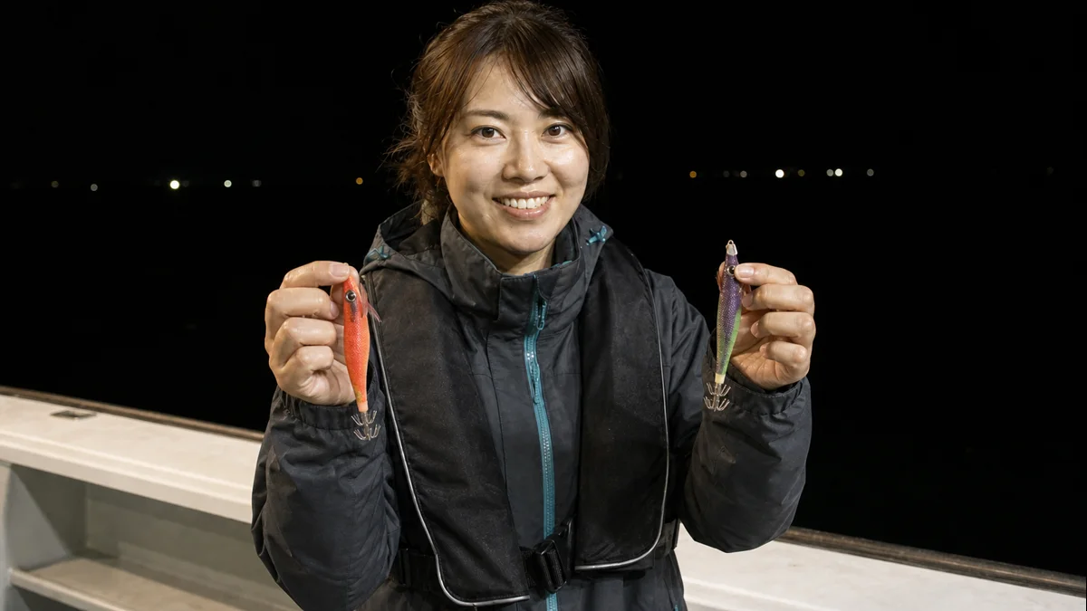夜の遊漁船で色違いのエギを両手に持って見比べる女性